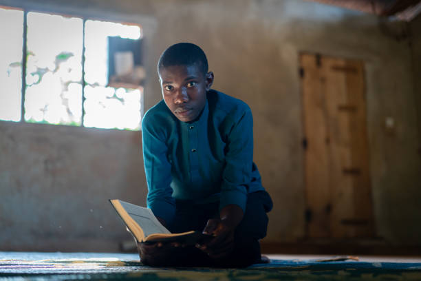 African teenage boy sitting and reading book in poor school stock photo