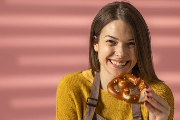 Portrait of a beautiful young woman holding a tasty pretzel while standing against pink background.