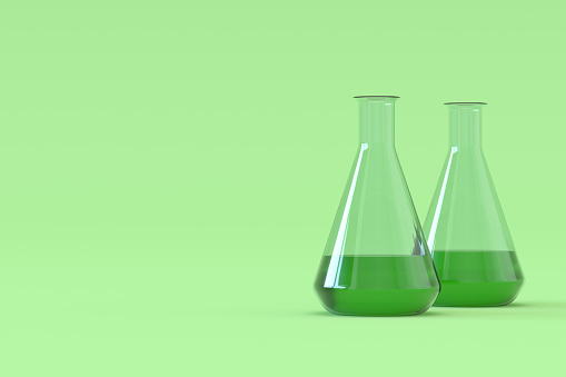 Display of a green liquid sample being poured from a  measuring cylinder into a volumetric flask with other equipment in the background