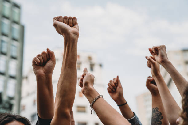 personas con los puños en alto en una manifestación en la ciudad - antirracismo fotografías e imágenes de stock