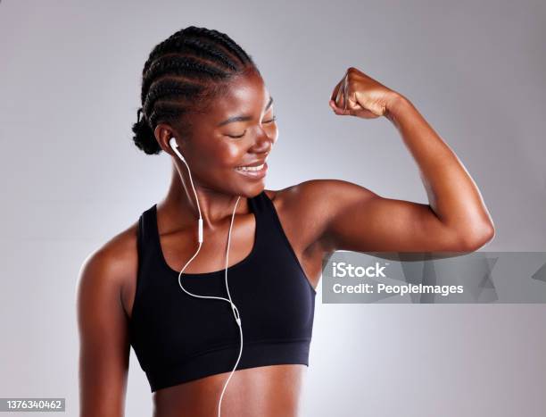 Studio Shot Of A Sporty Young Woman Wearing Earphones And Flexing Her Arms Against A Grey Background Stock Photo - Download Image Now
