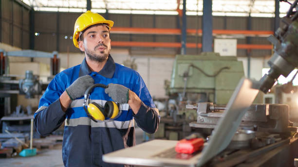 istock Engineer worker in uniform feeling tired and exhaust during work in front of machine in the factory. Put safety earmuff on machine. Manufacturing facility working and technology. Industrial concept 1376345395