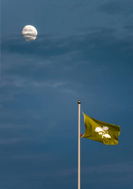 eine national trust-flagge weht hoch auf einem kornischen dach, mit dem silbernen mond, der dahinter vor einem dunkler werdenden himmel scheint. - cornish flag stock-fotos und bilder