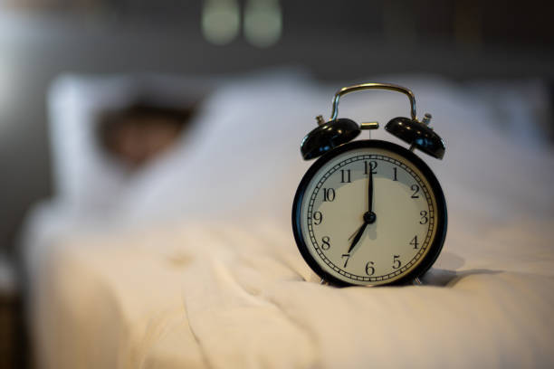 istock Alarm clock on the bed with sleeping woman behind. 1376362279