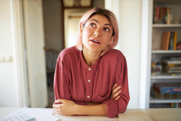 istock Cute student girl learning online, passing exam via webcam virtual video conference call, sitting at table, looking up with pensive thoughtful facial expression. People, education and technology 1376381273