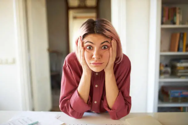 Photo of Funny surprised bug eyed young woman with nose ring and pinkish hair looking at camera in full disbelief, holding hands on her face, shocked with astonishing unbelievable news, being lost for words