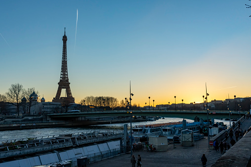 Eiffel Tower at sunset with tourists and locals in the foreground. This is along the banks of the Seine in Paris, France, Europe.