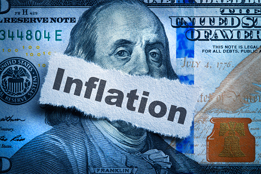 Inflation printed on a piece of torn paper that rests on top of the portrait of Benjamin Franklin on the one hundred dollar bill.