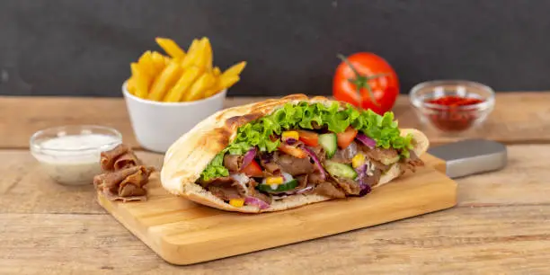 Döner Kebab Doner Kebap slice fast food in flatbread with French Fries on a wooden board panorama sliced