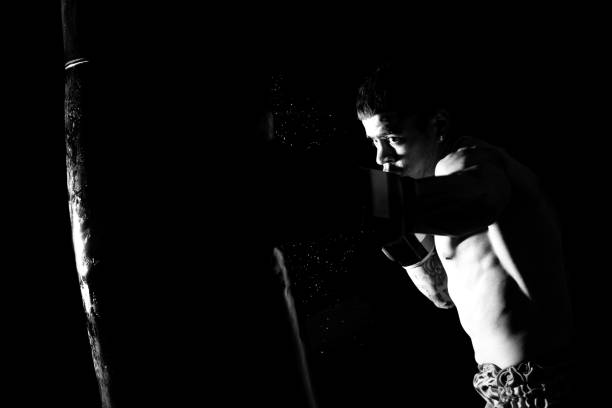 Young man hits a punching bag over black background.