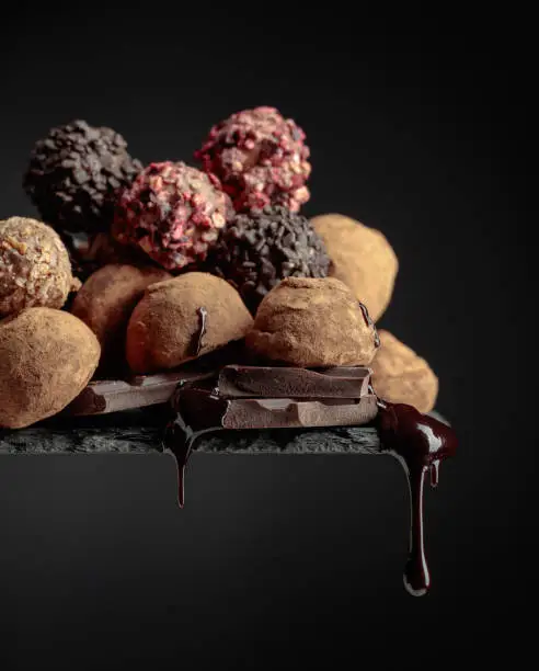 Delicious chocolate truffles and falling drops of chocolate sauce on a black background.
