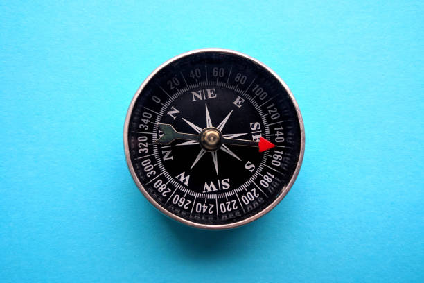 Metal magnetic compass with red arrow on blue background. Top view. stock photo