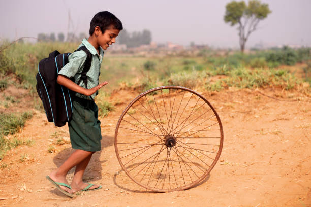 Poor child of Indian ethnicity running bicycle Tyre on country road.