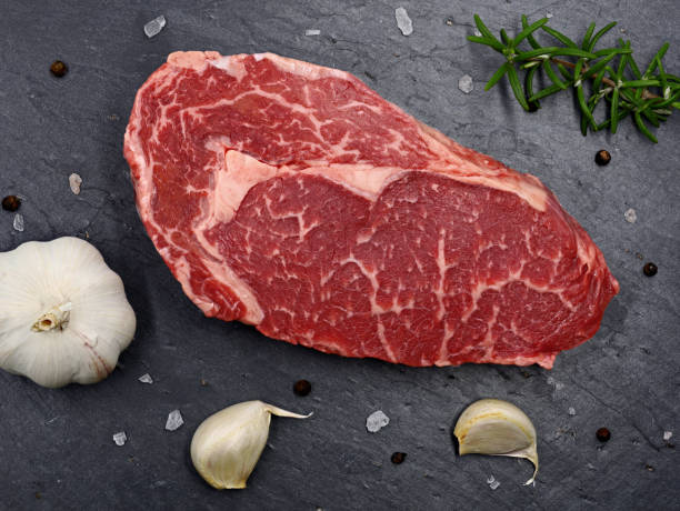 carne cruda jaspeada steak ribeye en plato de pizarra negra, vista superior de carne de res fresca a la barbacoa con especias - carne black angus fotografías e imágenes de stock