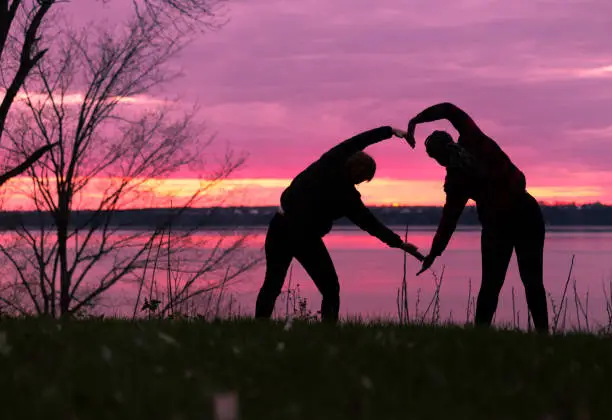 Photo of Two peoples forming a heart shape with sunset silhouette