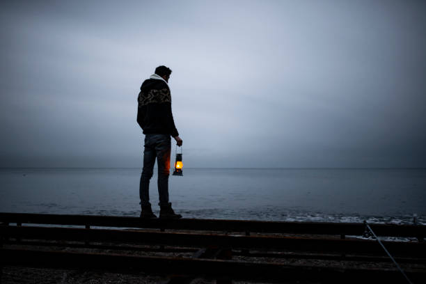 istock young man standing on the beach in cold weather, holding lighthouse, looking at horizon. 1376507358