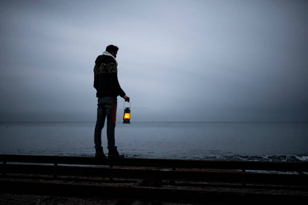istock young man standing on the beach in cold weather, holding lighthouse, looking at horizon. 1376507885