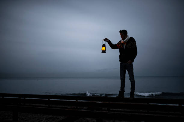 istock young man standing on the beach in cold weather, holding lighthouse, walking. 1376508546
