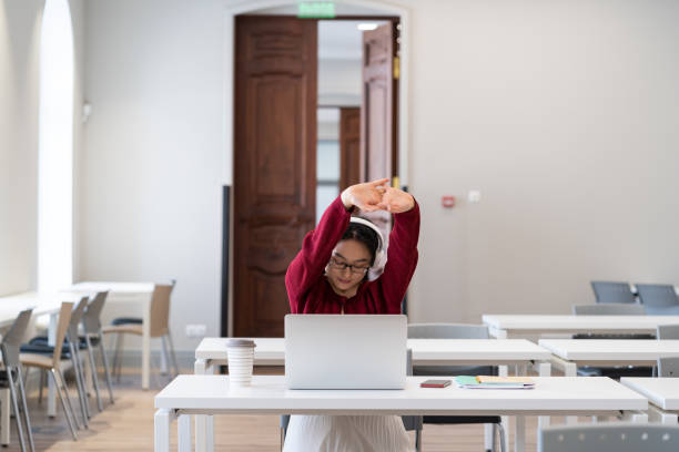 junges asiatisches mädchen erholt sich während der arbeit am laptop im coworking space und streckt die arme, um die belastung zu lindern - recreate stock-fotos und bilder