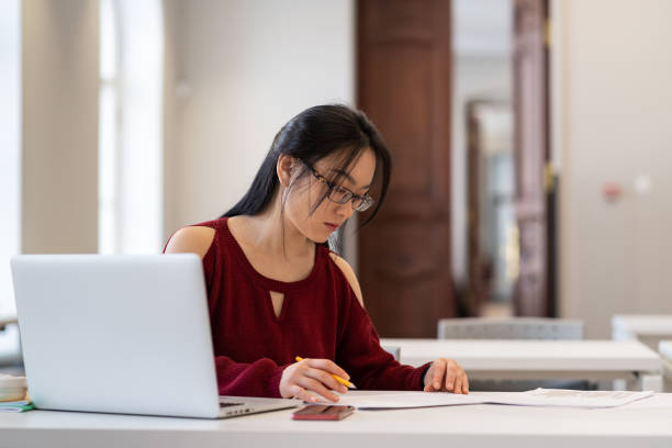 istock Focused asian female student preparing for exam or doing homework in university reading room 1376511072