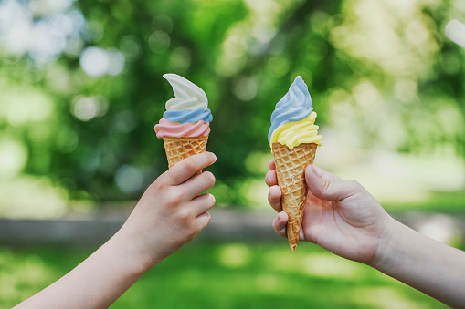 Two cones with creamy ice cream with the colors of the Ukrainian and Russian flags in children's hands. Symbol of friendship and peace. Summer vacation photos. Horizontal photo.