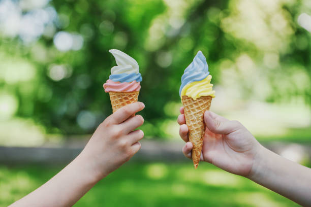 two cones with creamy ice cream with the colors of the ukrainian and russian flags in children's hands. symbol of friendship and peace. summer vacation photos - mayıs fotoğraflar stok fotoğraflar ve resimler