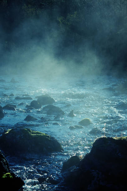 Charm of morning mist. Haze and spray on rapids of mountain river. Ray of morning sun breaks through foggy milk