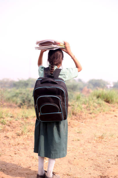 Elementary age poor child walking on country road holding book on head