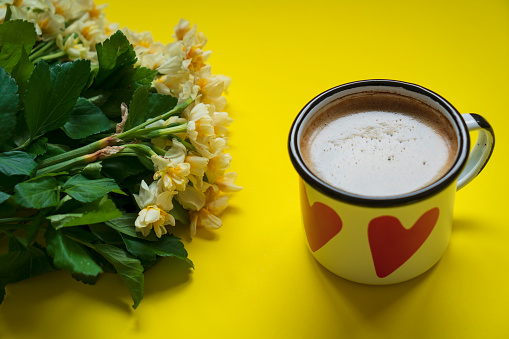 Morning cup of coffee and spring daffodil flowers on yellow background.Beautiful breakfast for Women day, Mother day.