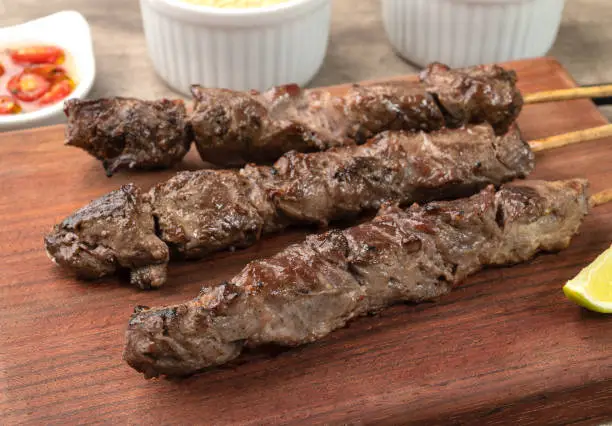 Photo of Meat skewers over wooden board with farofa, lemon and pepper