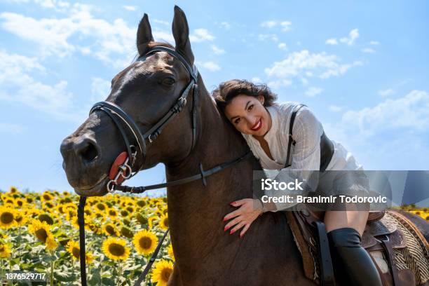 Cheerful Brunette Horseback Riding She Is Wearing Traditional White Dress And Long Black Boots Rural Scene Sunny Day Sunflower Field In Background Stock Photo - Download Image Now