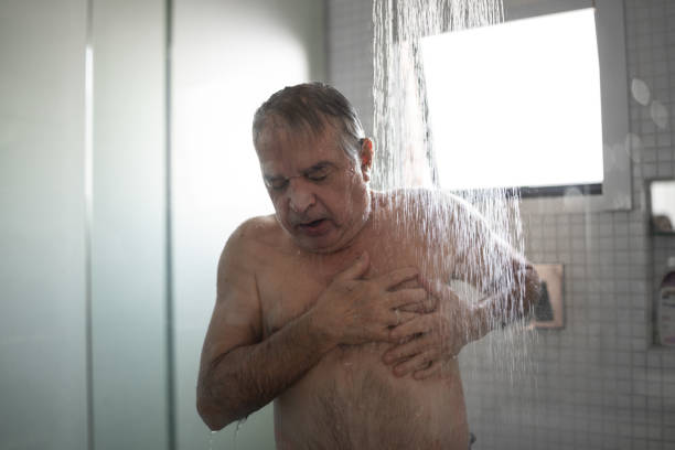 uomo anziano che sente dolore al petto mentre fa la doccia - men naked water male foto e immagini stock