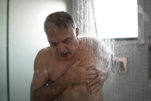 uomo anziano che sente dolore al petto mentre fa la doccia - men naked water male foto e immagini stock