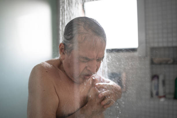 uomo anziano che sente dolore al petto mentre fa la doccia - men naked water male foto e immagini stock