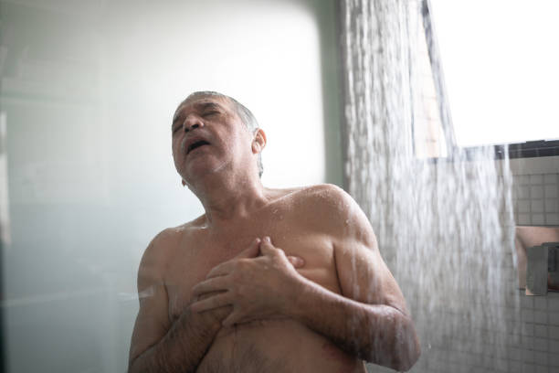 uomo anziano che sente dolore al petto mentre fa la doccia - men naked water male foto e immagini stock
