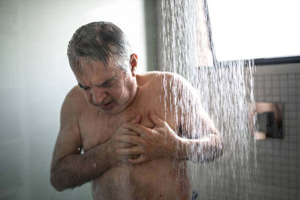 uomo anziano che sente dolore al petto mentre fa la doccia - men naked water male foto e immagini stock