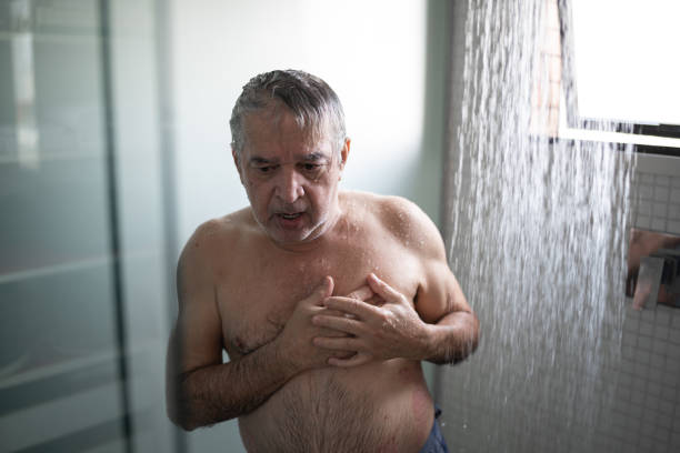 uomo anziano che sente dolore al petto mentre fa la doccia - men naked water male foto e immagini stock