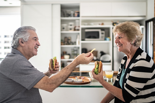 Happy senior couple eating burguer at home