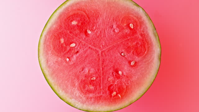 SLO MO LD Half of a watermelon rotating on a light red surface