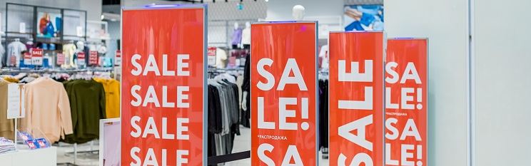 Sale sign at the entrance to clothing store,large red panels with white words. Seasonal discount offer in store.