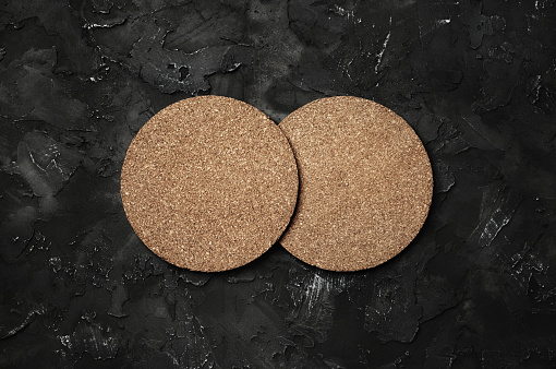 Two blank cork beer coasters on black stone background. Responsive design template. Flat lay.
