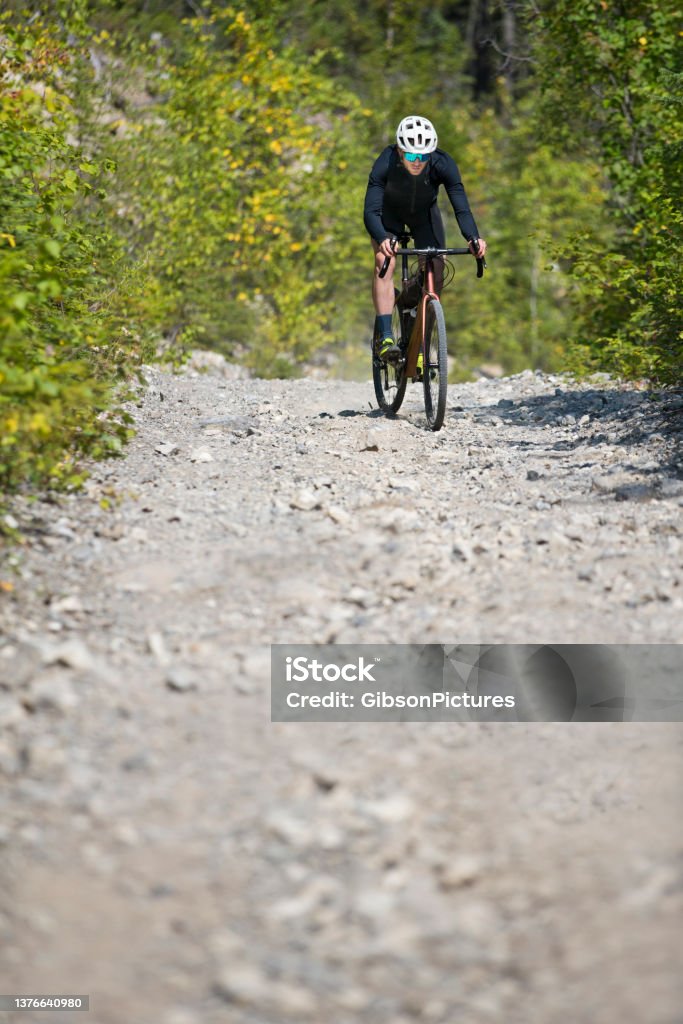 Gravel Bike Downhill Ride A man rides his gravel bike on a steep downhill while on a backcountry bicycle ride. Gravel bikes are similar to cyclo-cross bicycles with sturdy wheels and tires for riding on rough terrain. He has a frame bag attached to his bike to carry extra gear. Bicycle Stock Photo
