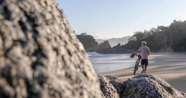 istock Man pushes mountain bike down beach, at sunrise 1376646820