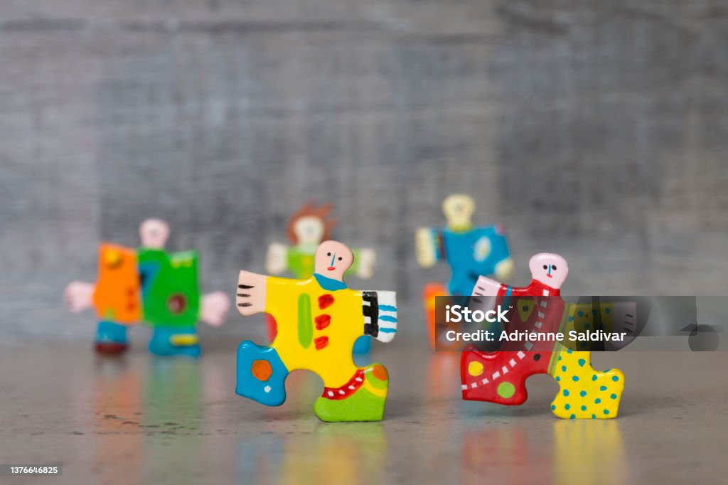 Hand painted jigsaw puzzle piece figures Hand-painted jigsaw puzzle piece figures representing people in bright colors arranged on a table top with a gray textured wood background. Concept of friendship, acceptance, individuality, and diversity. Creativity Stock Photo