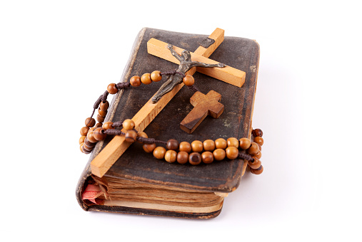 Old dusty prayer book, a cross and a rosary laying on top of it Christianity Catholicism traditional religious symbols, group of objects detail, closeup, nobody. Christian Catholic symbolism concept