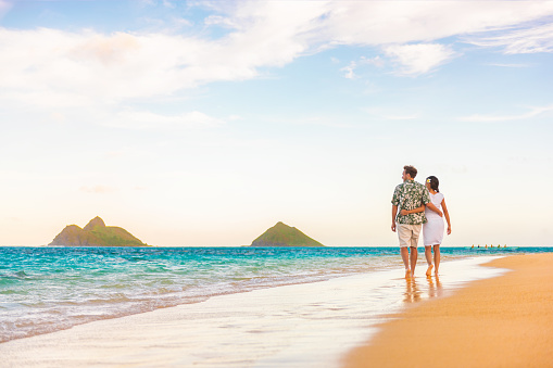 Hawaii beach vacation couple walking at sunset luxury travel holiday honeymoon destination. Newlyweds happy on Lanikai beach, Oahu, Hawaii.