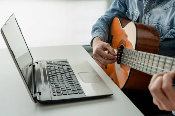 istock MAN LEARNING TO PLAY GUITAR ONLINE WITH LAPTOP AT HOME. VIDEO TUTORIAL CONCEPT. 1376682941