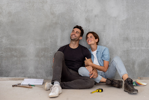 Happy couple taking a break from building their house and sitting on the floor thinking about the decoration and smiling