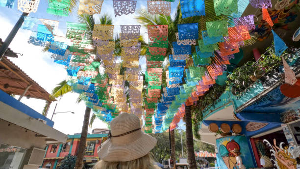 Tourist walking under papel picado (perforated paper) flags.