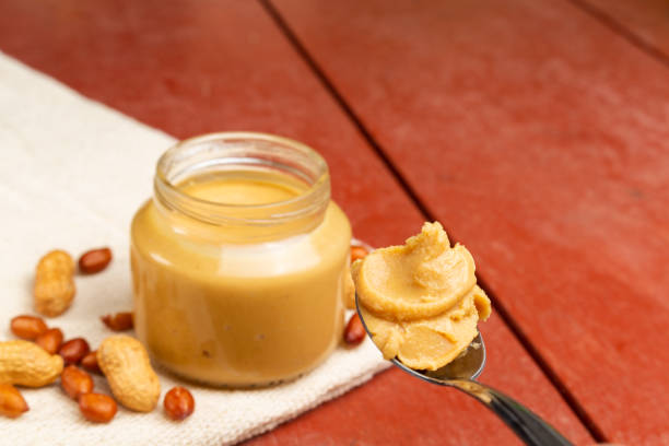 Spoon of peanut butter on breakfast table at farm Open peanut butter jar on a red wooden table with a spoon full of peanut butter TEASPOON OF PEANUT BUTTER stock pictures, royalty-free photos & images